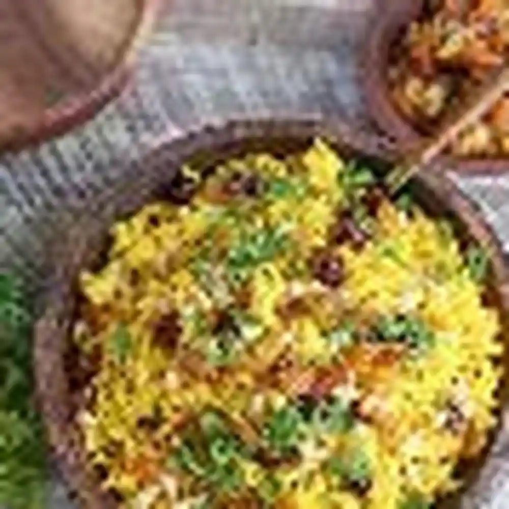 Golden yellow kabseh rice with meat and herbs in rustic clay bowl