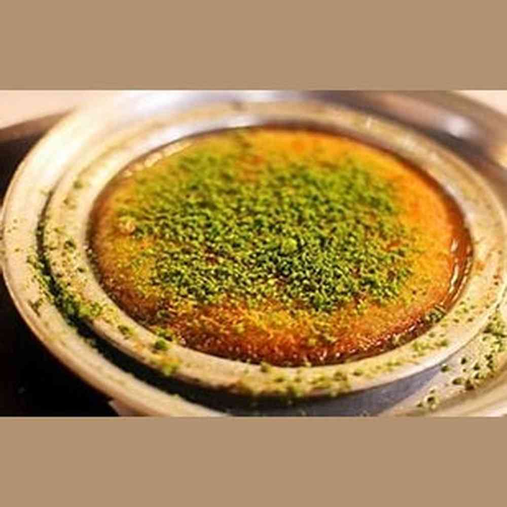 Golden-brown kunafa dessert with syrup sheen and chopped green pistachios in rustic ceramic dish
