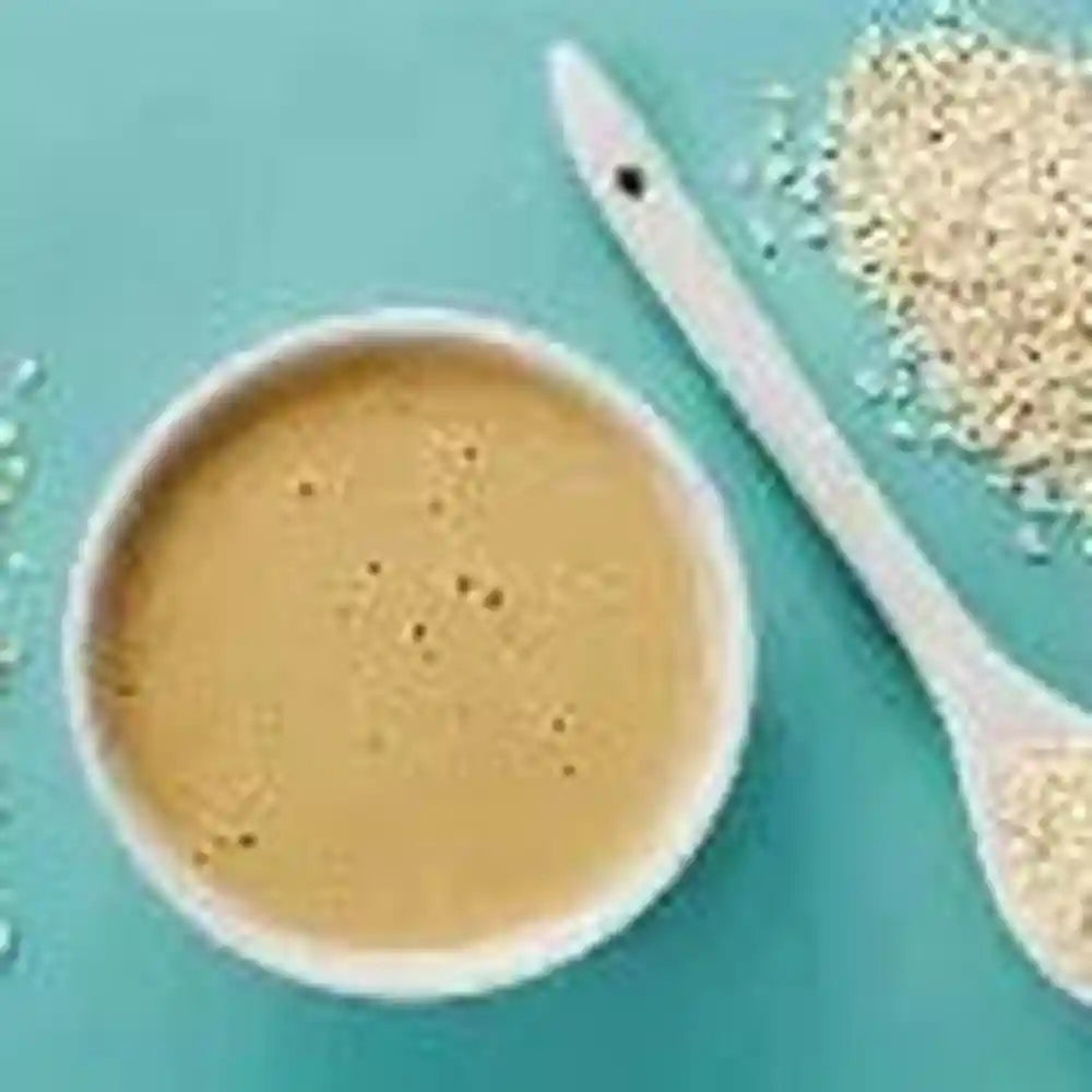 creamy light beige tahini with toasted sesame seeds in white bowl on teal background